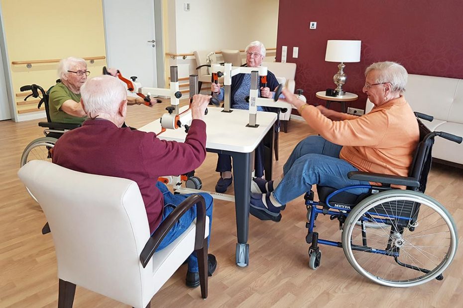 Vier Senioren bewegen sich am Plaudertisch, zwei Frauen sitzen dabei im Rollstuhl