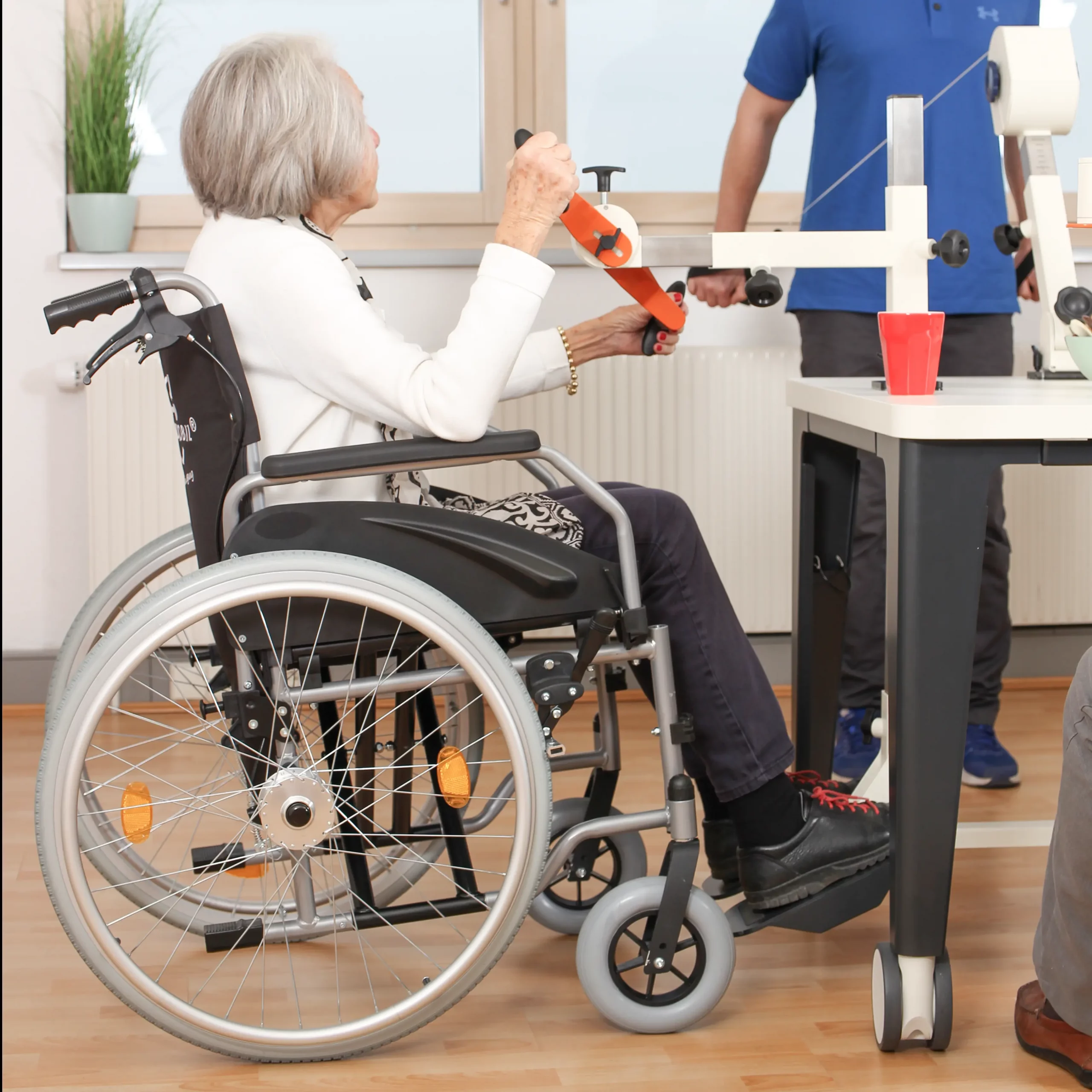 Seniorin sitzt im Rollstuhl am Plaudertisch und bedient die Drehorgel